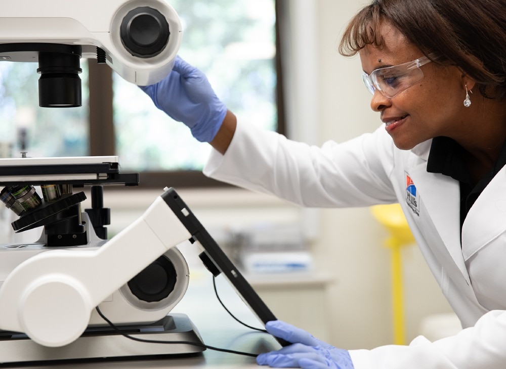 白衣と保護メガネを着用し、研究所で顕微鏡を使用している女性科学者。