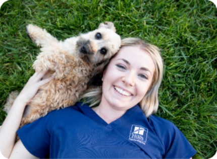 A small dog lying in the grass next to a Hill's researcher